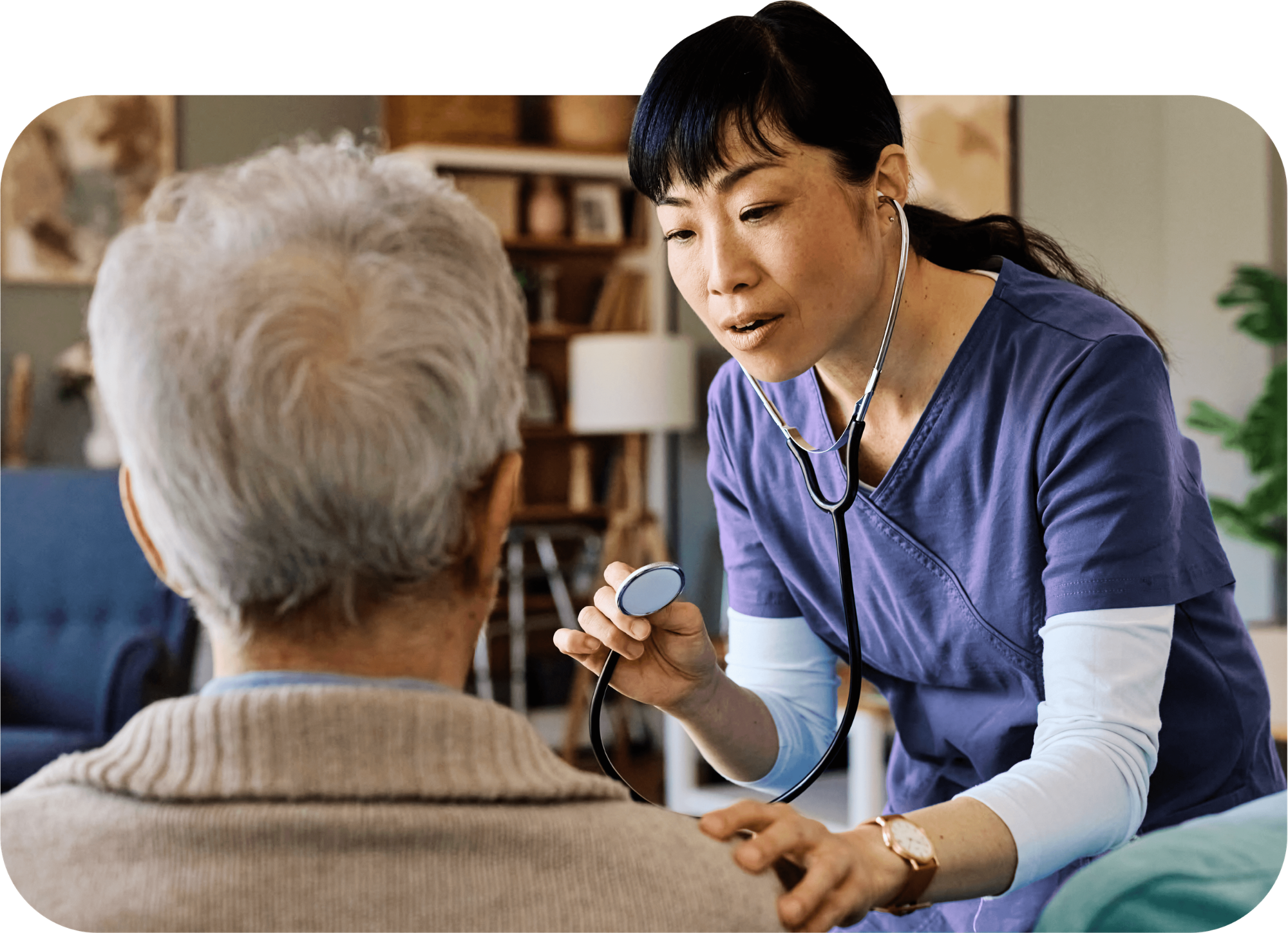 A WellBe RN in purple scrubes holds her stethoscope to examine an older female patient